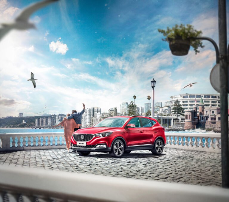 Auto MG ZS rojo junto a una pareja a orillas del mar